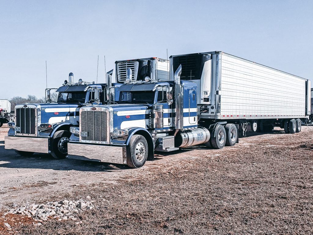 2 blue semi trucks with white stripes side by side